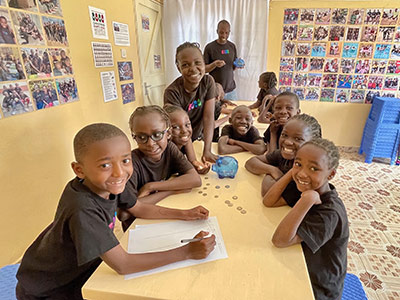 Children Sitting at a Table with Coins and a Piggy Bank