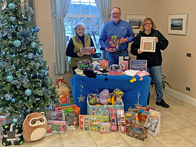 Three People Holding Wrapped Gifts with Toys Around a Table